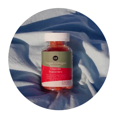 Bottle of vegan collagen gummies laying on a blue cloth with sun rays falling on it.