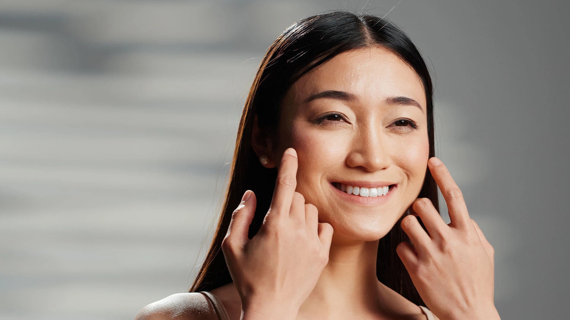 Joyful woman smiling while gently pulling at her cheek to emphasize skin firmness and elasticity, under soft lighting. Represents youthful skin, collagen support, and anti-aging benefits through skincare or nutritional wellness.