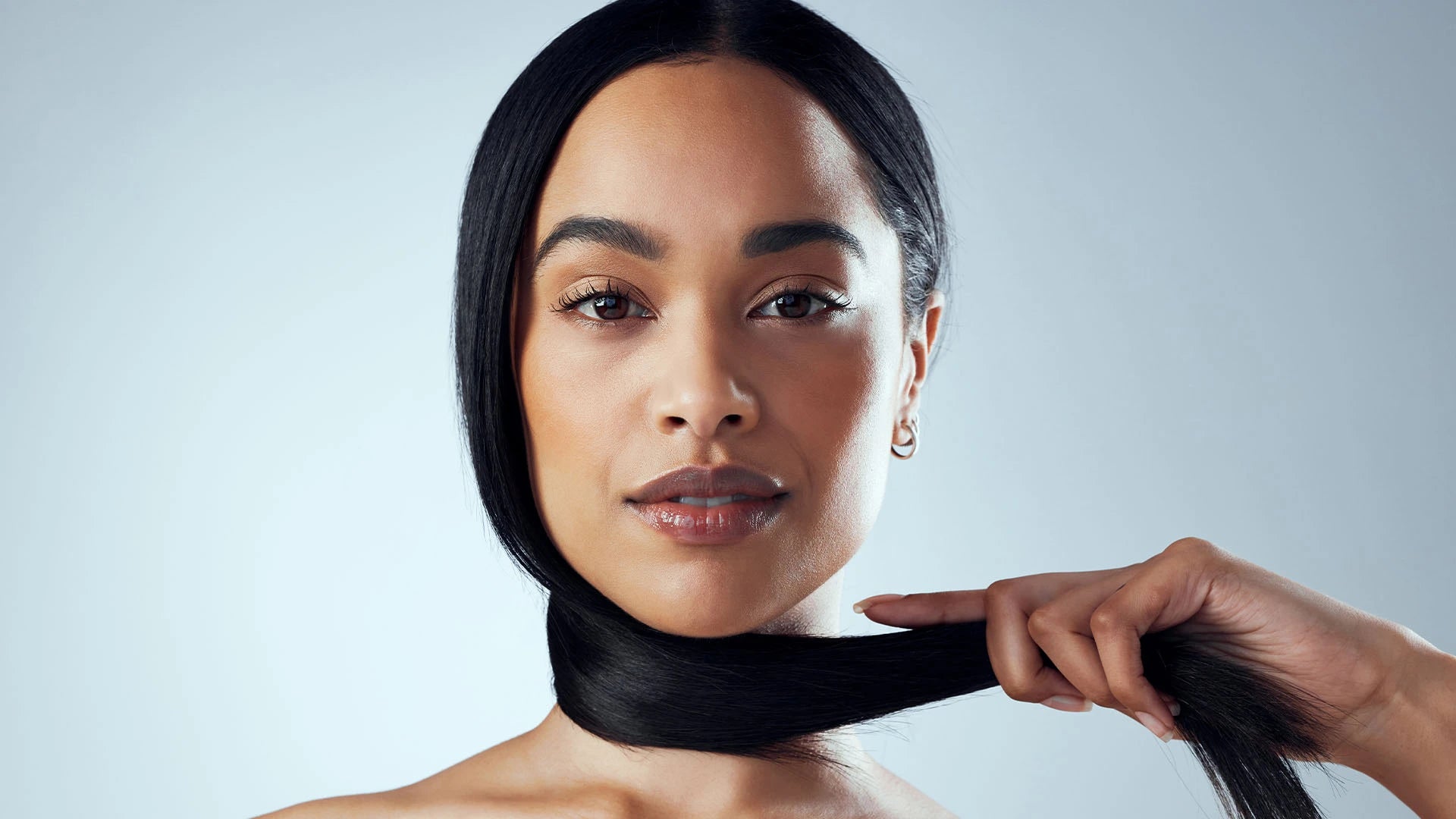 Close-up of a confident woman with sleek, shiny black hair wrapped around her neck, showcasing hair strength, vitality, and smoothness. Ideal visual for promoting hair care, protein-rich beauty supplements, or shine-enhancing treatments